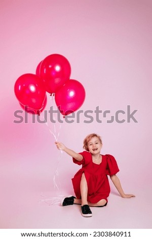 Child girl smiles toothlessly, wears a bright pink dress and carries balloons, has fun in a circle of friends, isolated on a pink background. Children, the concept of the holiday, birthday.