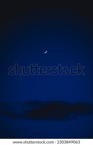 The narrow crescent of the moon and Venus nearby in the dark blue sky
