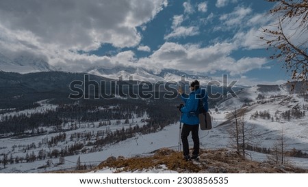 A girl in winter ski clothes photographs mountains in snow and forest. The girl is standing on a mountain.