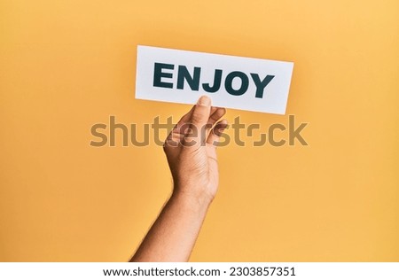 Hand of caucasian man holding paper with enjoy word over isolated yellow background