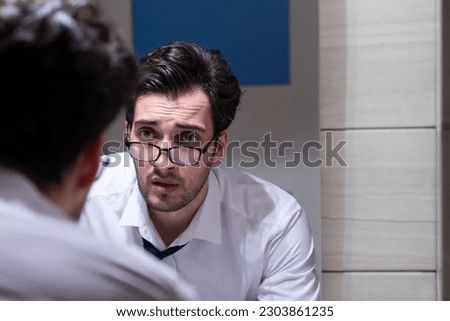 Aggressive businessman standing angry in front of mirror in the restroom after exhausting busy workday Royalty-Free Stock Photo #2303861235