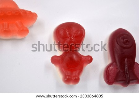 Bright sweet jelly candies, sweets in the form of red, yellow aliens, cherry space rockets, green astronauts, pink alien alien ships and an orange planet, asteroids.