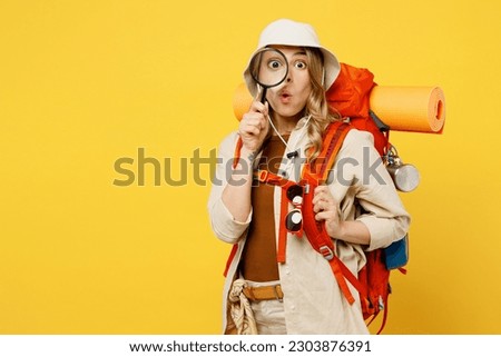Young woman carry backpack with stuff mat looking camera on you use magnifier isolated on plain yellow background Tourist leads active lifestyle walk on spare time Hiking trek rest travel trip concept Royalty-Free Stock Photo #2303876391