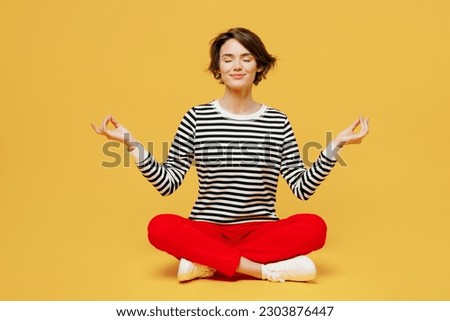 Full body spiritual young woman wear casual black and white shirt sit hold spreading hands in yoga om aum gesture relax meditate try calm down isolated on plain yellow color background studio portrait Royalty-Free Stock Photo #2303876447