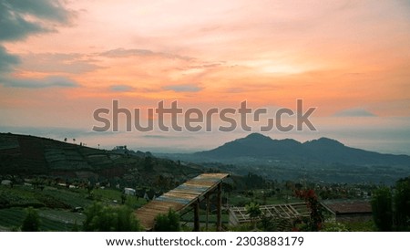 Beautiful reddish orange sunrise sky with mountain range and plantation on the foreground -  Mangli Sky View Tourist attraction on slope  Sumbing Mountain, Indonesia