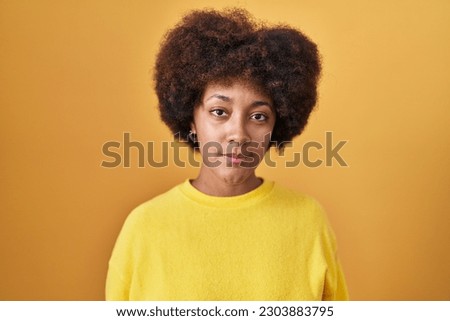 Young african american woman standing over yellow background relaxed with serious expression on face. simple and natural looking at the camera. 