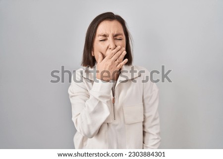 Middle age hispanic woman standing over isolated background bored yawning tired covering mouth with hand. restless and sleepiness. 