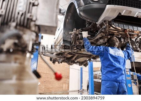 Car mechanic inspecting car steering rod and repair suspension detail. Lifted automobile at repair service station. replacement of ferrule and leverage Royalty-Free Stock Photo #2303894759