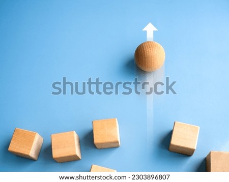 Leadership, business success, unique, difference, challenge, and motivation concepts. Wooden sphere rolling fastest, leading with rising arrow and following with wood cube blocks on blue background. Royalty-Free Stock Photo #2303896807