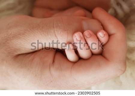 Close-up of a small hand of a child and the hand of mother and father. A newborn baby after birth holds tightly, squeezes the thumb of its parents. 