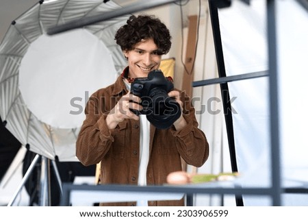 Happy photographer guy taking professional photos of various desserts in modern photostudio, young man using digital camera, making photo shoot for cooking blog