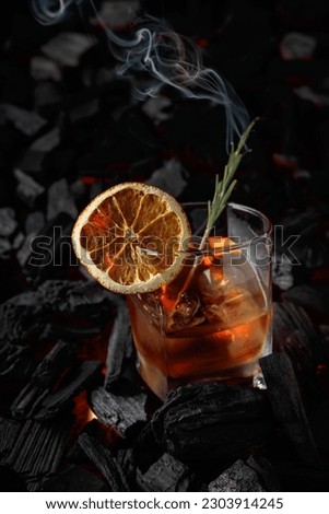 Old-fashioned cocktail with ice, dried orange slice, and rosemary. Whiskey with rosemary and beautiful swirls of smoke on a background of burning charcoal. Royalty-Free Stock Photo #2303914245