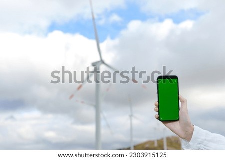 Close-up of a smartphone with a green screen in the hand of a female engineer against the background of wind turbines