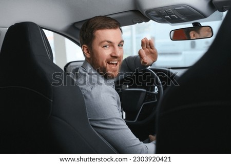 Taxi driver smiling while turning over to the backseat looking talking with clients. Successful businessman husband looking at the backseat at dealer shop before buying a car. Royalty-Free Stock Photo #2303920421