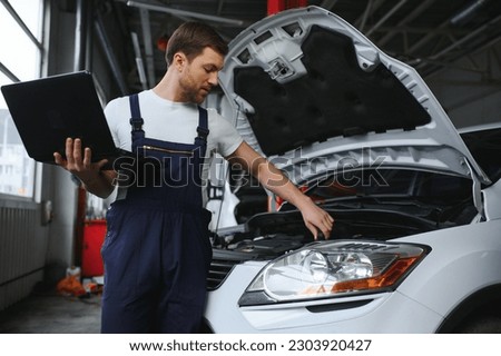 Mechanic man mechanic manager worker using a laptop computer checking car in workshop at auto car repair service center. Engineer young man looking at inspection vehicle details under car hood. Royalty-Free Stock Photo #2303920427