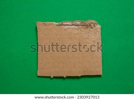 Ripped cardboard paper piece on green background with copy space.