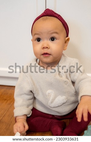 A baby girl sitting on the floor, playing with teething toy.