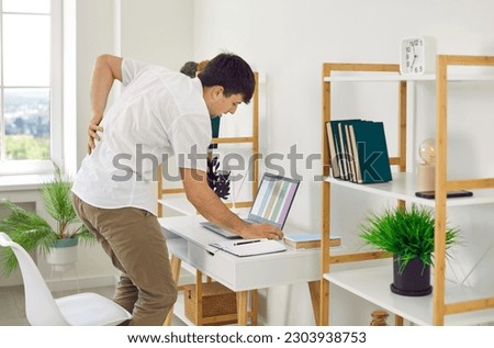 Young man starts feeling negative effects of sedentary lifestyle. Young guy gets very tired and exhausted and has intense lumbago back pain after working at computer desk with laptop PC for long time Royalty-Free Stock Photo #2303938753