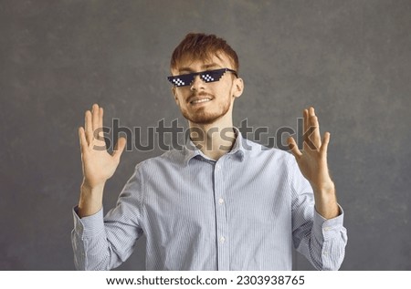 Funny guy with ginger hair having fun. Studio headshot portrait of happy young man in cool pixelated thug life meme glasses standing against grey background