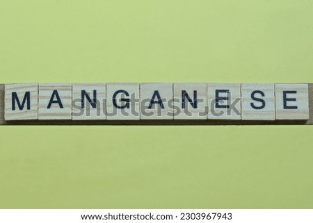 the word manganese of gray small wooden letters lies on a yellow table
