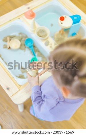 Little girl playing with kinetic sand and wooden toys. Sensory development and experiences, themed activities with children, fine motor skills development. High quality photo