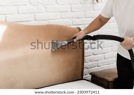 Dry wash cleaner is removing dirt and dust from bed headboard using dry cleaning extraction machine. Process of extraction dirt from headboard of bed using extractor cleaning machine Royalty-Free Stock Photo #2303972411