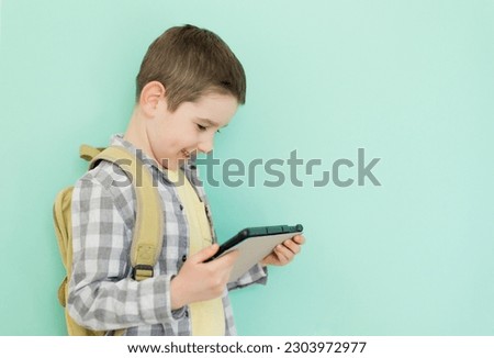 Caucasian boy with school backpack holding tablet on a green background with copy space