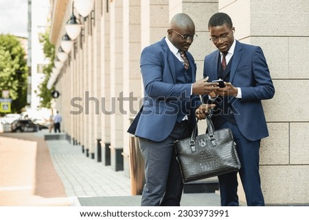 Two black African American businessmen friends in suits are talking while standing on the street. Outdoor business meeting Royalty-Free Stock Photo #2303973991