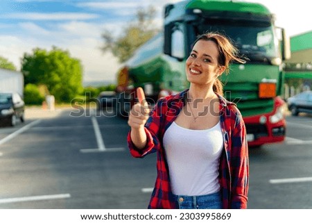 Junior female truck driver standing in front of her truck after she successfully completed her first tour thumps up for a job well done Royalty-Free Stock Photo #2303995869