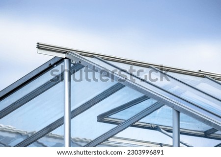 Greenhouse made of glass and metal framing is under bright blue sky, background photo