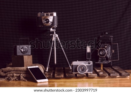 A still life with several vintage cameras on wood and fabrics and a smartphone