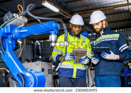 Supporting Engineer team, african american and caucasian man use laptop to control and testing Artificial Intelligent welding robotic automatic arm machine in modern factory. industry 4.0 Technology.