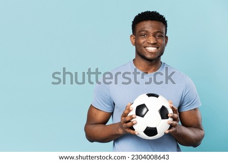 Smiling african american man holding soccer ball isolated on blue background, copy space, advertising. Professional football player posing for picture