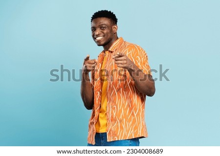 Handsome african american man in orange shirt standing isolated on blue background, pointing with fingers, looking at camera. Attractive male smiling, posing for picture, advertising