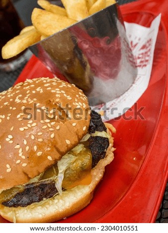 Delicious hamburger in bun with french fries, all on red underlay.