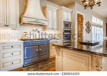 Elegant french country style kitchen with blue cast iron oven marbled countertops soft yellow wood cupboards gleaming hardwood floors  Royalty-Free Stock Photo #2304016353