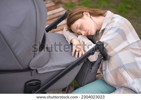Tired young Caucasian woman, overtired mother by sleepless nights, snoozing in newborn carriage while walking in a green park. Lack of energy, exhaustion, fatigue. Maternity concept. people. lifestyle Royalty-Free Stock Photo #2304023023