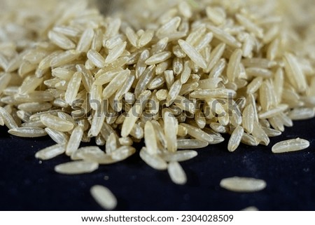 Studio macro shot of a pile of brown rice, also called complete, integral or wholegrain rice, with a blurred background. Brown rice is richer in fiber and used in several diets. Royalty-Free Stock Photo #2304028509