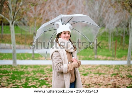 Preteen girl with an umbrella smiling and looking at camera outdoors in autumn.