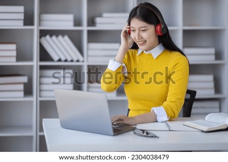Young adult happy smiling Hispanic Asian student wearing headphones talking on online chat meeting using laptop in university campus or at virtual office. College female student learning remotely.
