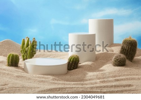 Three white podiums in round and cylinder-shaped are displayed on the beach sand with Cacti. Blank space to promote product Royalty-Free Stock Photo #2304049681