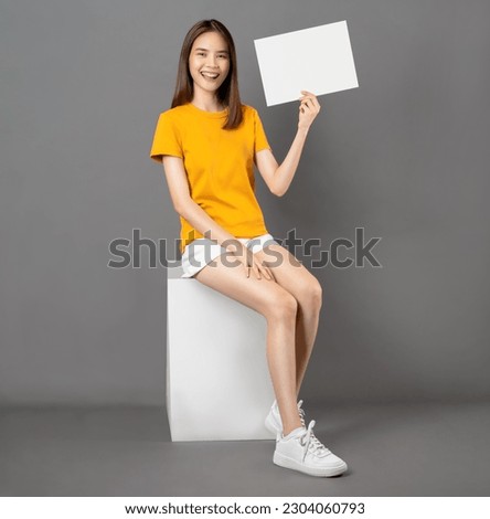 Smiling Asian woman sitting on box and hand holding paper speech bubble on white background, empty space for text on ads.