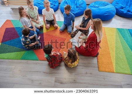 Reading time in an elementary school or kindergarten, a teacher reading a book to children in an elementary school or kindergarten. The concept of pre-school education. Selective focus Royalty-Free Stock Photo #2304063391