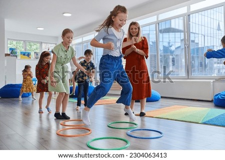 Small nursery school children with female teacher on floor indoors in classroom, doing exercise. Jumping over hula hoop circles track on the floor. Royalty-Free Stock Photo #2304063413