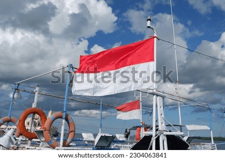 the Indonesian flag is flying on the mast of a fishing boat that is leaning in the harbor