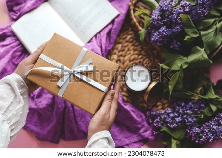 Gift box with a bow in hands on a spring background.