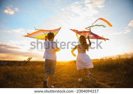Brother and sister playing with kite and plane at the field on the sunset