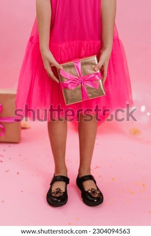 Close up of a girl holding a gift box with a pink silk ribbon, giving a gift for a holiday. Merry Christmas, Happy New Year, Valentine's Day, holiday, festive, Birthday, surprise concept.
