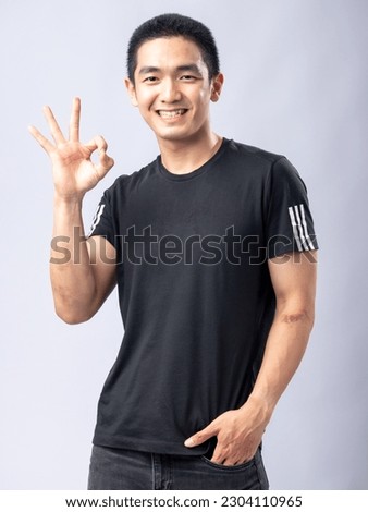 A portrait of an Asian man wearing a black shirt while making displaying the OK hand sign. Isolated with a white background.