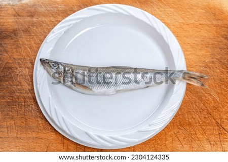 Small raw silverfish on a white plastic plate on a wooden table. Top view.